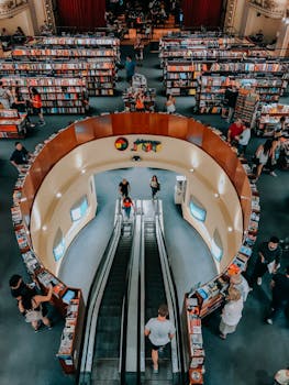 A busy indoor bookstore with people browsing shelves and riding escalators.